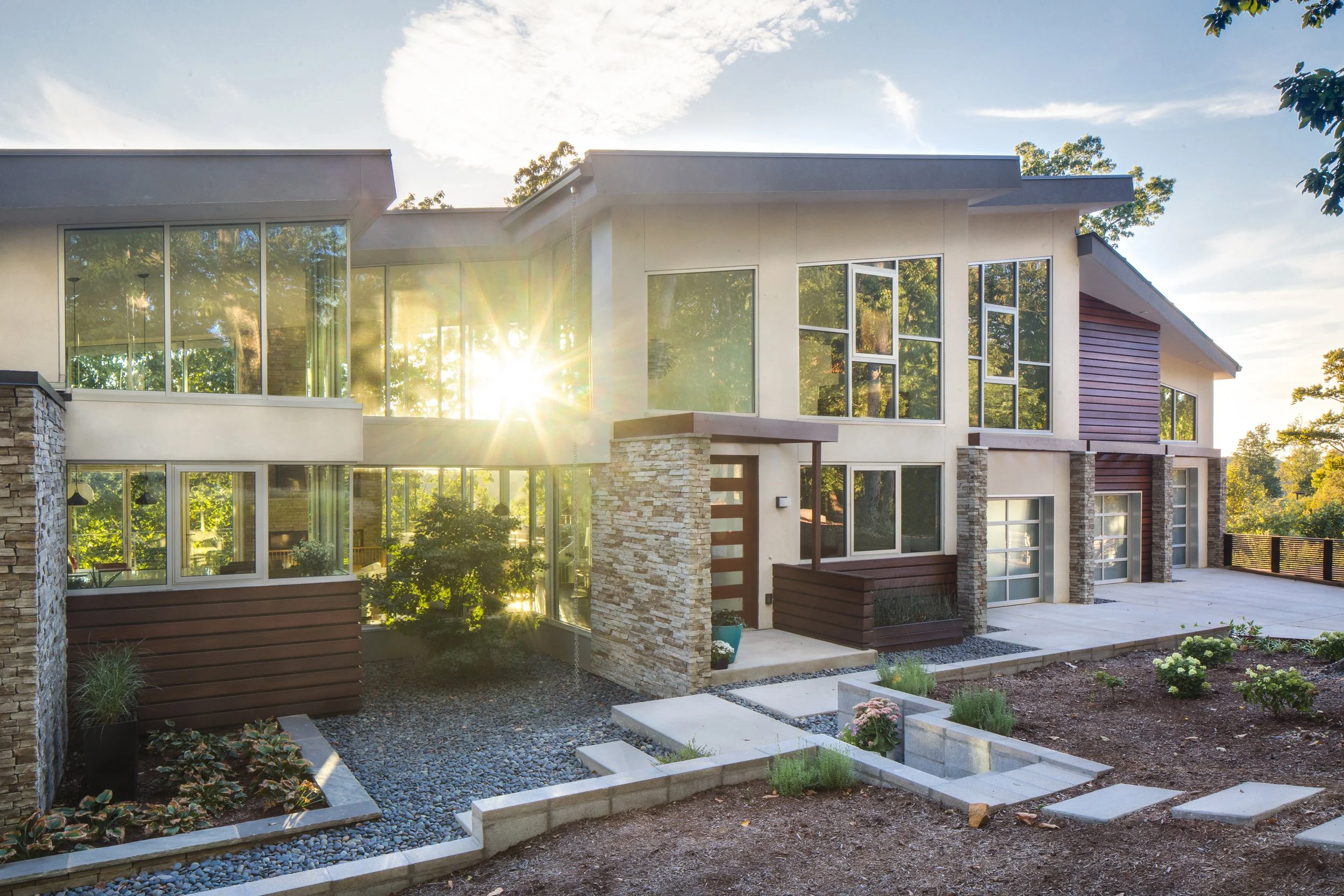 Sunlit modern home with large windows, stone walls, and mature trees
